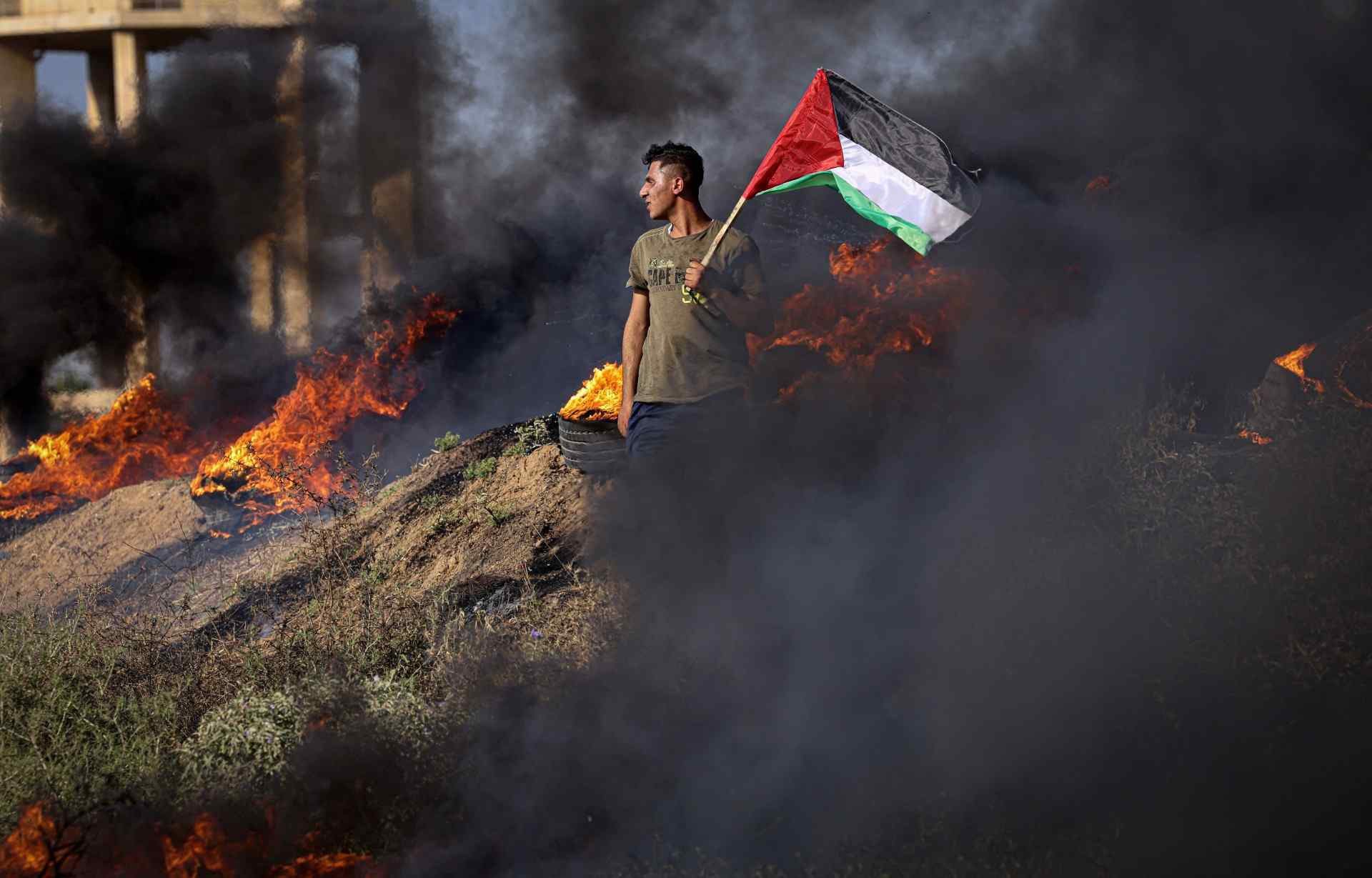 Palestino ostenta bandeira perto de pneus em chamas, em protesto a leste de Gaza